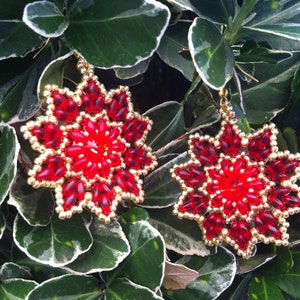 Pode incluir: Um par de brincos de estrela vermelha e dourada com um design de contas. Os brincos são feitos com pequenas contas vermelhas e contas douradas.