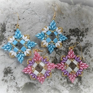 Op de afbeelding: Drie paar geknoopte oorbellen in een stervorm. De oorbellen zijn gemaakt met witte, blauwe, roze en paarse kralen. De oorbellen hangen aan gouden haakjes.