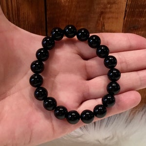 May include: A black beaded bracelet with round, smooth beads. The bracelet is on a person's hand.