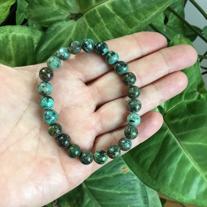 May include: A turquoise gemstone bracelet with dark brown markings. The bracelet is made of round beads and is strung on elastic.