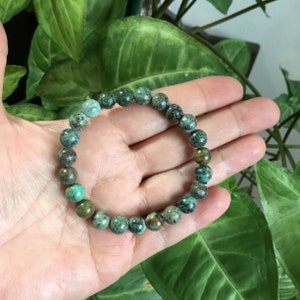 May include: A turquoise gemstone bracelet with round beads. The bracelet is made of natural stones and has a green and brown color.