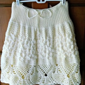 Puede incluir: Una falda de crochet blanca con un delicado patrón de encaje y un lazo en la cintura.