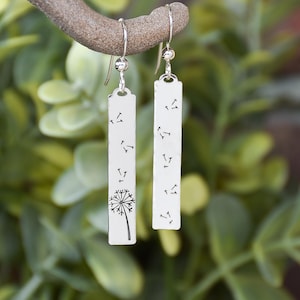 May include: Silver dangle earrings with a dandelion design. One earring features a dandelion with seeds blowing in the wind, while the other earring features only the seeds blowing in the wind.