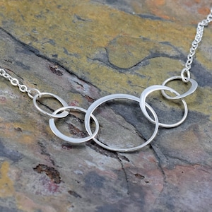 May include: A silver necklace with five interlocking circles. The circles are of varying sizes and are connected to a silver chain.