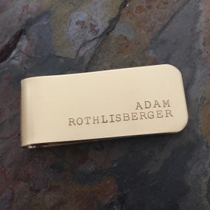 May include: A gold-coloured metal money clip with the name "Adam Rothlisberger" engraved on it.