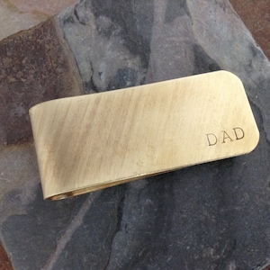 May include: A gold-coloured metal money clip with the word "DAD" engraved on it.