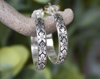 May include: A pair of silver hoop earrings with a floral design. The earrings are small and delicate, and they would make a great gift for a friend or loved one.