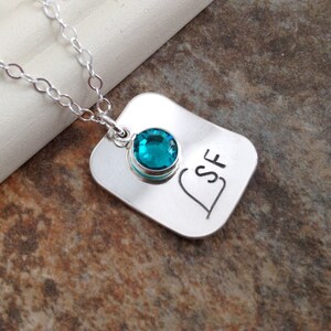 May include: Silver necklace with a rectangular pendant featuring the initials "LSF" and a teal blue gemstone.