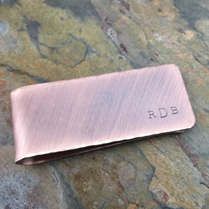 以下が含まれることがあります： 前面に「RDB」の刻印が施された、ブラシ仕上げの銅製のマネークリップです。