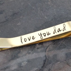 May include: Gold tie bar with the inscription "love you dad" engraved on it.