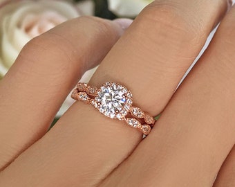 May include: Rose gold engagement ring set with a round center stone and a halo of smaller stones. The band is a delicate twisted design.