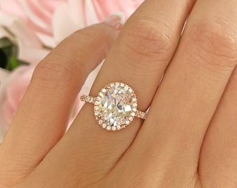 May include: A rose gold engagement ring with a large oval-shaped center stone surrounded by a halo of smaller stones. The ring is set on a thin band.