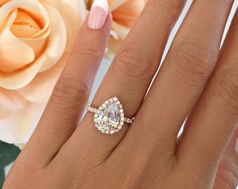 May include: A pear-shaped engagement ring with a halo setting. The ring is set in rose gold and features a large, clear center stone.