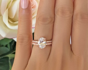 May include: A rose gold engagement ring set with an oval-shaped center stone and a matching band with smaller stones.