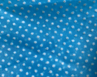 May include: Close-up of a bright blue fabric with a pattern of small, evenly spaced white polka dots. The fabric has a slightly textured appearance, and the dots are soft and blurred.
