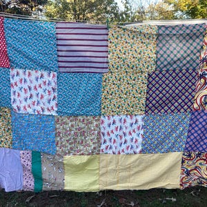 May include: A patchwork quilt with a variety of patterned fabrics, including polka dots, stripes, floral, and geometric designs. The quilt is displayed outdoors, hanging on a clothesline, showcasing a mix of colors and textures.