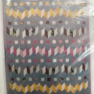 May include: A gray quilt with a geometric pattern of alternating chevrons and squares. The chevrons are in shades of yellow, white, pink, and floral prints. The quilt is encased in plastic.
