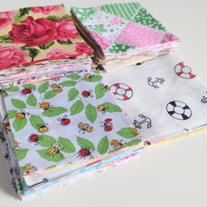May include: Four stacks of fabric squares with different patterns. The first stack has a floral pattern with pink roses on a yellow background. The second stack has a patchwork pattern with pink, green, and white squares. The third stack has a white background with red and black anchor and life preserver designs. The fourth stack has a white background with green leaves and red ladybugs.