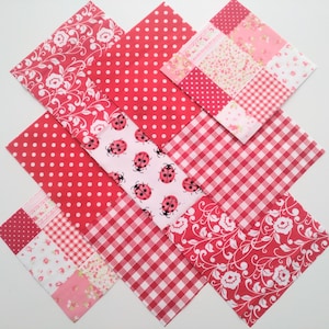 May include: A diamond arrangement of red and white fabric squares. The fabrics display diverse patterns such as polka dots, floral designs, gingham checks, and ladybugs. The color scheme is predominantly red and white, with touches of pink.