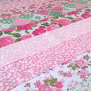 May include: A pink and white patchwork quilt featuring floral patterns. The quilt is made from different fabrics with various floral designs, including roses, leaves, and small floral prints. The quilt is sewn together in a horizontal pattern, creating a striped effect.