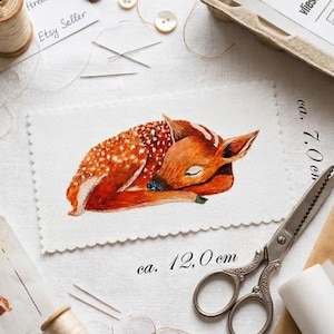 Könnte beinhalten: Aquarell-Illustration eines schlafenden Fohlens, ca. 12 cm lang, auf weißem Stoff. Das Bild ist von Nähutensilien umgeben, darunter Schere, Faden, Knöpfe und ein Bügeleisen. Der Text "Etsy Seller" ist sichtbar.