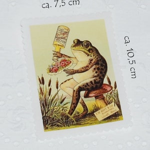 Könnte beinhalten: Eine Vintage-Illustration eines Frosches, der auf einem Pilz sitzt, eine Flasche Schnaps und einen Blumenstrauß hält. Das Bild ist auf einem weißen Stoffquadrat mit einem gewellten Rand gedruckt. Der Text "Emil Horr & Co. Pommernstr. 120.  Levin, Meckl." ist in der rechten unteren Ecke des Bildes gedruckt.