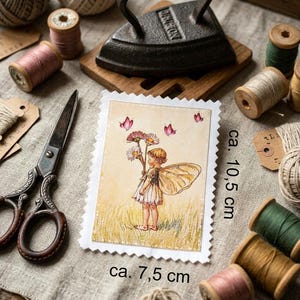 Könnte beinhalten: Vintage Illustration einer Fee, ca. 7,5 x 10,5 cm, mit gezacktem Rand. Das Bild ist von Nähutensilien umgeben, darunter Garnrollen, eine Schere und ein antikes Bügeleisen. Das Bild hat eine Vintage-Ästhetik.