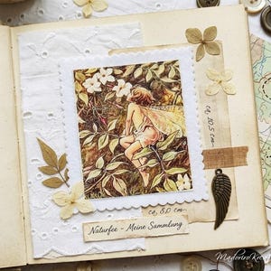 Könnte beinhalten: Eine Vintage-Scrapbook-Seite mit einer Feenillustration, getrockneten Blumen und dekorativen Elementen. Das Feenbild ist mit einem weißen, gezackten Rand umrahmt. Die Seite enthält einen kleinen Metallflügel-Anhänger und den Text "Naturfee - Meine Sammlung".