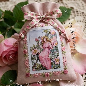 Könnte beinhalten: Ein hellrosa Stoffbeutel mit Kordelzug und einer rechteckigen Illustration einer Figur in einem rosa Kleid, umgeben von Blumen. Der Beutel ist mit gestickten rosa Rosen und einem Band verziert. Text auf dem Beutel gibt 10,5 cm mal 7,0 cm an.