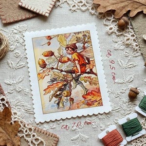 Può includere: Illustrazione di una fata su una carta con bordo smerlato, circa 9,5 cm per 7,0 cm, con una fata e ghiande. L'immagine è circondata da materiali artigianali a tema autunnale, come rocchetti di filo e foglie secche.