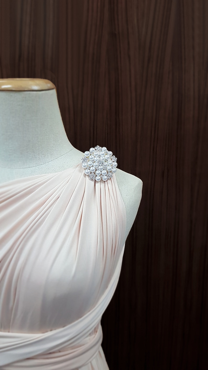 K&ouml;nnte beinhalten: Hellrosa Kleid mit einer Perlen- und Strassbrosche. Die Brosche ist rund und hat mehrere kleine Perlen und klare Strasssteine. Das Kleid ist drapiert und hat ein One-Shoulder-Design.