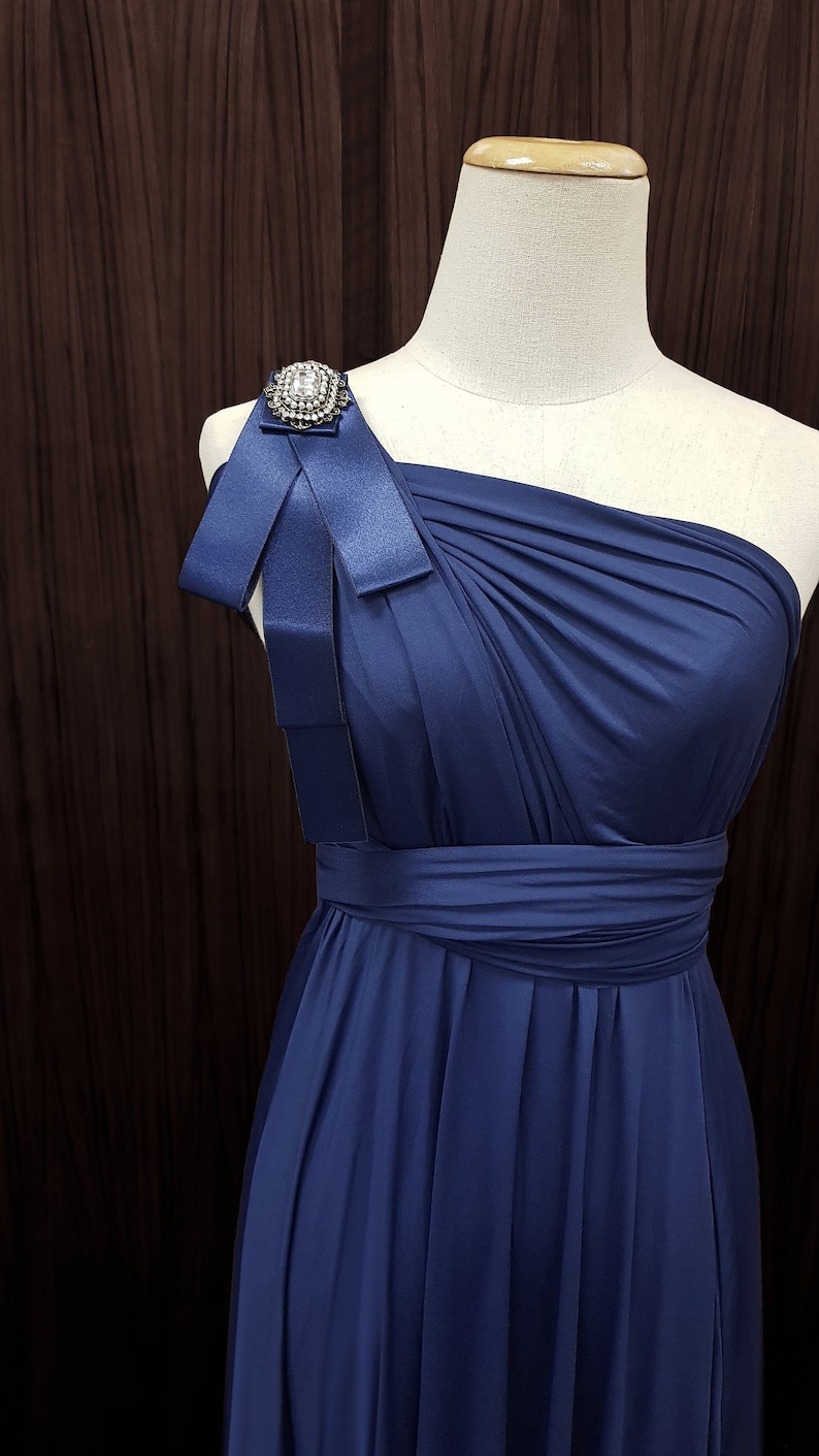 Puede incluir: Un vestido azul marino de un solo hombro con un lazo de sat&eacute;n y un broche de pedrer&iacute;a en el hombro.