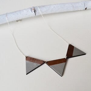 May include: A silver chain necklace with a geometric pendant made of three connected wooden triangles. The triangles are painted with a silver and brown colour scheme.