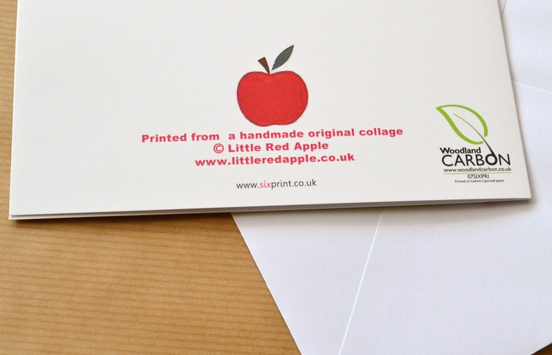 May include: Back of a greeting card with a red apple illustration and the text "Printed from a handmade original collage &copy; Little Red Apple www.littleredapple.co.uk www.sixprint.co.uk" and a green leaf logo with the text "Woodland CARBON www.woodlandcarbon.co.uk 07SXPR"