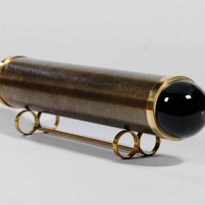 May include: A brass kaleidoscope with a black glass end cap, resting on a gold metal stand with three circular legs.