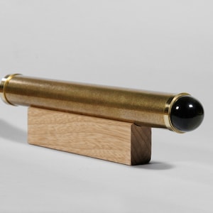 May include: A brass kaleidoscope with gold accents and a black lens, resting on a small wooden block. The cylindrical body has a textured finish. The kaleidoscope is a classic optical toy.