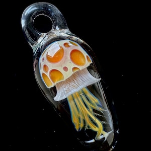 May include: A glass pendant featuring a mushroom with orange and white accents and a yellow and blue stem.