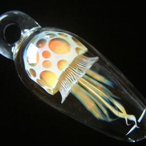 May include: A glass pendant shaped like a jellyfish with a white and orange bell and long, translucent tentacles.