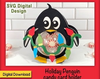 Può includere: SVG Digital Design - Porta biglietti di Natale a forma di pinguino per caramelle. Un pinguino nero con occhi bianchi e becco giallo tiene una ghirlanda di luci colorate con un cerchio trasparente al centro. Il pinguino è su uno sfondo di piastrelle bianche.
