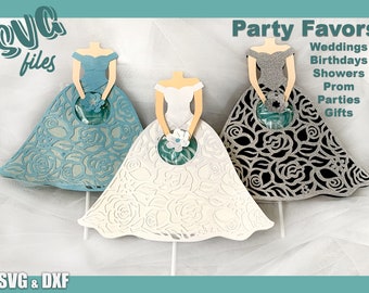 Può includere: Tre figure di sposa in carta con intricati disegni di rose, che tengono un contenitore rotondo per caramelle. Le spose sono vestite di blu, bianco e nero con accenti di glitter. Il testo "Party Favors" è in cima all'immagine, con le parole "Weddings, Birthdays, Showers, Prom Parties, Gifts" elencate sotto. Il testo "SVG & DXF" è in fondo all'immagine.