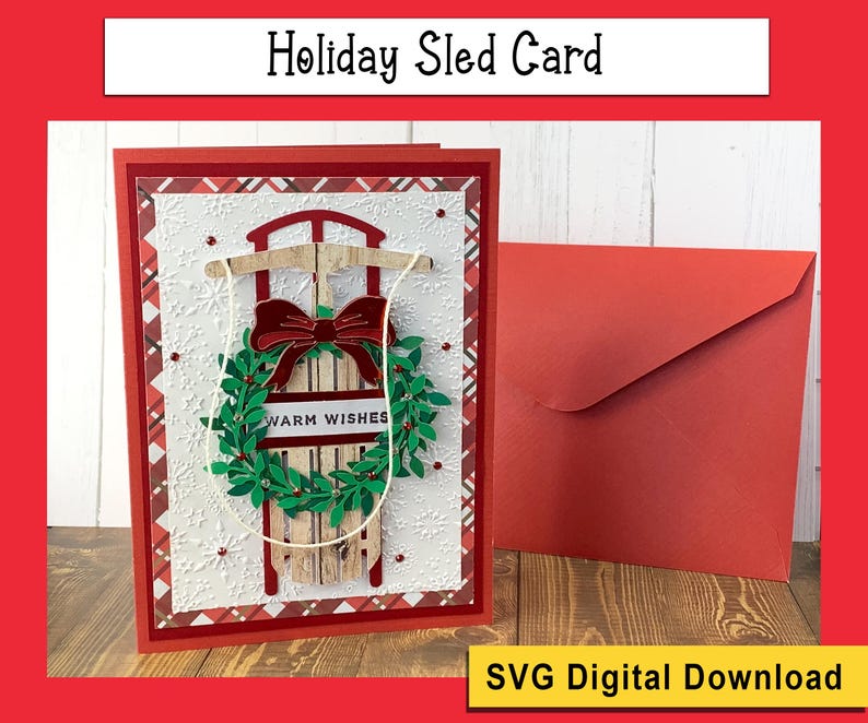 May include: A red and white plaid card with a wooden sled and a green wreath with the text "Warm Wishes". The card is accompanied by a red envelope.