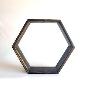 May include: A hexagonal wall shelf constructed from dark stained wood with a visible grain texture. The frame features six equal sides forming a geometric shape with a hollow center, showcasing a weathered finish with lighter brown highlights.