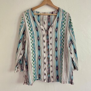May include: A white button-up shirt with a blue, green, and pink geometric pattern. The shirt has a V-neck and three-quarter sleeves.