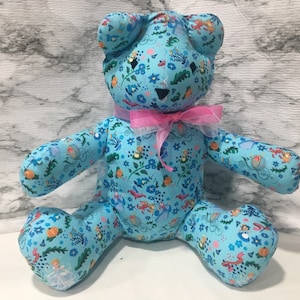 May include: A blue teddy bear with a pink bow. The bear is covered in a pattern of flowers, birds, and other whimsical designs.