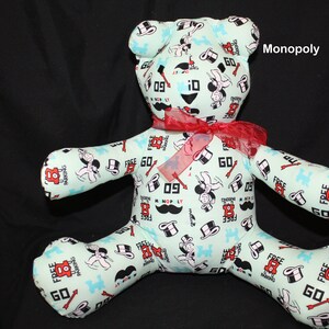 May include: A plush teddy bear with a Monopoly theme. The bear is light blue with a red bow and is covered in Monopoly game pieces, including the Monopoly man, dice, and the words "Free Parking".