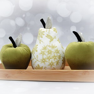 May include: Three decorative fruit cushions in a wooden tray. A green velvet apple cushion, a green velvet apple cushion, and a white pear cushion with a floral pattern and a hummingbird design.