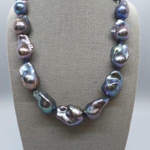 May include: A necklace featuring a series of large, irregularly shaped baroque pearls. The pearls exhibit a dark, iridescent luster with deep purple, blue, and charcoal gray tones, strung together to form a continuous strand of organic, textured beads.
