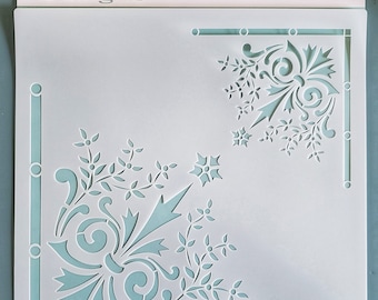 Può includere: Uno stencil bianco con due disegni d'angolo che presentano intricati motivi floreali. Lo stencil è realizzato in un materiale sottile e flessibile ed è progettato per essere utilizzato con la vernice. Lo stencil è etichettato "Boutique Paint Designs".