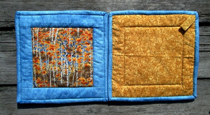 May include: Two blue and yellow quilted pot holders with a fall-themed fabric square in the center of one pot holder.