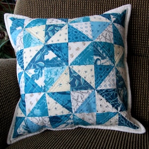 May include: A blue and white patchwork pillow with a white border. The pillow is made of various fabrics with different patterns, including floral, geometric, and polka dot.